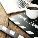 Movie clapper with laptop and cup of coffee on wooden background